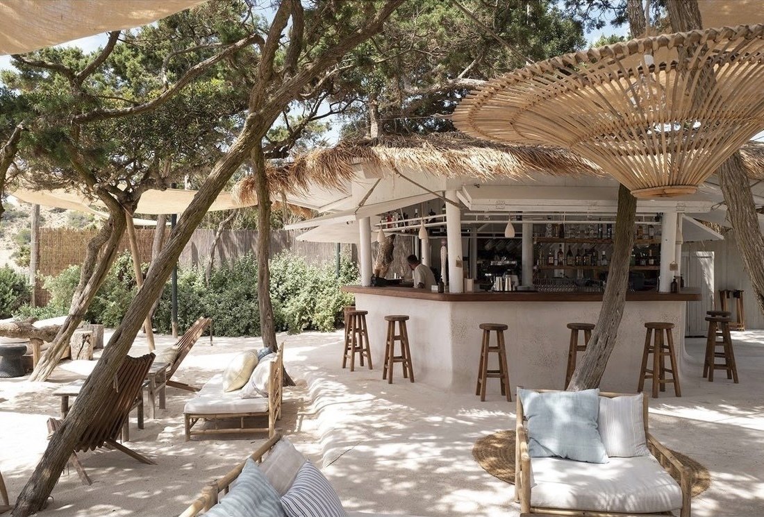 Bohemian beach bar with wooden stools under pine trees in Ibiza